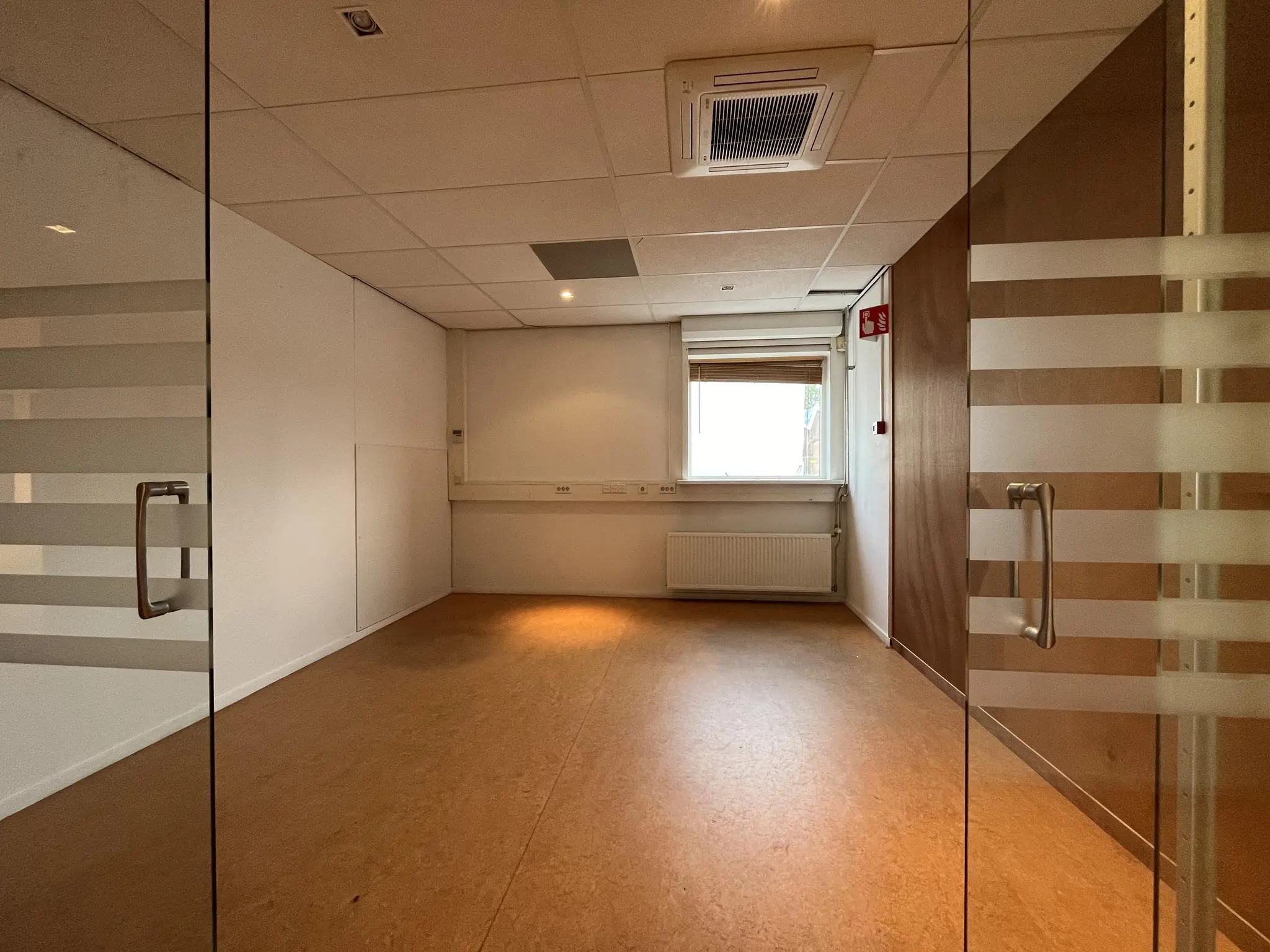 Leeg kantoor met glazen deuren aan de 2e Daalsedijk, voorzien van systeemplafond en raam met jaloezieën.